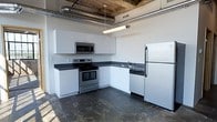 Located at 340 SW 5th St in the heart of downtown Des Moines, Iowa, this single-floor loft-style unit showcases a compelling blend of industrial character and modern functionality. The space features exposed overhead ductwork and raw ceiling details that lend an authentic urban warehouse aesthetic, a hallmark of the building's converted industrial roots.

The kitchen is a standout feature, outfitted with white cabinetry, dark countertops, and a full suite of stainless steel appliances, including an electric range, over-the-range microwave, dishwasher, and refrigerator. The L-shaped layout maximizes efficiency while offering ample counter and storage space. Dark, matte flooring throughout grounds the space and complements the industrial overhead elements, creating a cohesive, contemporary look.

The open layout and high ceilings contribute to an airy, spacious atmosphere that is characteristic of loft living. The overall ambiance strikes a balance between raw, industrial design and clean, modern finishes — ideal for those who appreciate urban living with functional, well-appointed interiors. The downtown Des Moines location places residents within close proximity to local dining, entertainment, and professional districts.