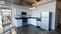 Located at 340 SW 5th St in the heart of downtown Des Moines, Iowa, this single-floor loft-style unit showcases a compelling blend of industrial character and modern functionality. The space features exposed overhead ductwork and raw ceiling details that lend an authentic urban warehouse aesthetic, a hallmark of the building's converted industrial roots.

The kitchen is a standout feature, outfitted with white cabinetry, dark countertops, and a full suite of stainless steel appliances, including an electric range, over-the-range microwave, dishwasher, and refrigerator. The L-shaped layout maximizes efficiency while offering ample counter and storage space. Dark, matte flooring throughout grounds the space and complements the industrial overhead elements, creating a cohesive, contemporary look.

The open layout and high ceilings contribute to an airy, spacious atmosphere that is characteristic of loft living. The overall ambiance strikes a balance between raw, industrial design and clean, modern finishes — ideal for those who appreciate urban living with functional, well-appointed interiors. The downtown Des Moines location places residents within close proximity to local dining, entertainment, and professional districts.