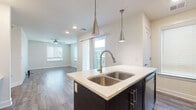This well-designed single-floor residence offers a thoughtful open-concept layout that seamlessly connects the kitchen and living areas. The kitchen is a standout feature, showcasing dark espresso cabinetry, light quartz countertops, and a bold navy blue island with a double stainless steel sink. Sleek pendant lights hang above the island, complementing the stainless steel appliances, including a range, microwave, and refrigerator. A tile backsplash adds a refined touch, while wood-look flooring runs throughout the main living areas, creating a warm and cohesive aesthetic. The open living room is bright and airy, benefiting from multiple windows with blinds and a sliding glass door that leads to a private balcony, flooding the space with natural light. A ceiling fan provides comfort throughout the room. The bedroom is generously proportioned, featuring plush carpeting, a ceiling fan, and access to a dedicated walk-in closet, offering ample storage. The bathroom is clean and contemporary, finished with neutral tile, a soaking tub with a handheld shower fixture, and dark cabinetry for contrast. Overall, this residence combines modern finishes with a functional layout, delivering a comfortable and stylish living environment.