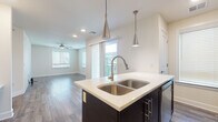This well-designed single-floor residence offers a thoughtful open-concept layout that seamlessly connects the kitchen and living areas. The kitchen is a standout feature, showcasing dark espresso cabinetry, light quartz countertops, and a bold navy blue island with a double stainless steel sink. Sleek pendant lights hang above the island, complementing the stainless steel appliances, including a range, microwave, and refrigerator. A tile backsplash adds a refined touch, while wood-look flooring runs throughout the main living areas, creating a warm and cohesive aesthetic. The open living room is bright and airy, benefiting from multiple windows with blinds and a sliding glass door that leads to a private balcony, flooding the space with natural light. A ceiling fan provides comfort throughout the room. The bedroom is generously proportioned, featuring plush carpeting, a ceiling fan, and access to a dedicated walk-in closet, offering ample storage. The bathroom is clean and contemporary, finished with neutral tile, a soaking tub with a handheld shower fixture, and dark cabinetry for contrast. Overall, this residence combines modern finishes with a functional layout, delivering a comfortable and stylish living environment.