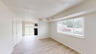 Located at 1224 W Breckenridge Dr in Mexico, Missouri, this two-story townhome offers a practical and well-organized layout across two equally sized floors. The main level features a bright living room with light hardwood-style flooring, crisp white walls, and a large window that allows natural light to fill the space. Adjacent to the living area, the kitchen is a standout with bold charcoal-gray cabinetry, light granite-style countertops, a double-basin sink, and a black electric range with a matching overhead hood — all complemented by the same light wood flooring and a window above the sink. A staircase connects the two levels, leading to the upper floor where both bedrooms are located. The primary bedroom features plush carpet, a wide window with outdoor views of the surrounding neighborhood, and a closet with built-in shelving and a hanging rod for ample storage. The second bedroom is equally cozy with soft carpet and neutral walls. The full bathroom is finished with a clean white tub-shower combination. Textured ceilings are consistent throughout the home, adding a classic residential character to each room.