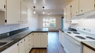 Located at 17840 32nd Avenue South in SeaTac, Washington, this single-floor unit offers a clean, functional layout with a variety of practical finishes throughout. The kitchen is a standout feature, equipped with white cabinetry, dark granite countertops, pendant lighting, a built-in peninsula, and white appliances including an electric range and refrigerator. Hardwood-style flooring runs through the kitchen and extends into the adjacent dining area, which benefits from a large window that invites natural light and views of the surrounding greenery. The living room continues the hardwood-style flooring and is warmed by baseboard heating along the exterior wall. The bedroom is carpeted for comfort and includes a generous closet with built-in shelving, providing ample storage. The bathroom features a wide vanity with under-cabinet storage, a light countertop, a large mirror with overhead lighting, and hardwood-style flooring. A dedicated in-unit laundry area accommodates a full-size washer and dryer side by side. Textured ceilings are present throughout the unit. The overall ambiance is bright, clean, and move-in ready, offering a practical and comfortable living environment in a convenient SeaTac location.