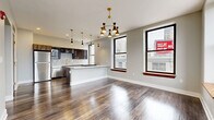 This thoughtfully designed 2-bedroom, 2-bathroom residence offers a seamless blend of modern aesthetics and urban living. The open-concept living and kitchen area serves as the heart of the home, anchored by rich hardwood flooring and abundant natural light streaming through large, black-framed windows that frame striking city views. The kitchen is a standout feature, showcasing dark wood cabinetry with gold hardware, a white quartz waterfall island, a white subway tile backsplash, stainless steel appliances, and a series of mid-century modern pendant lights that add a stylish focal point overhead. The primary bedroom is a spacious retreat with a ceiling fan, built-in closet, and large windows overlooking the urban skyline. The second bedroom also features hardwood floors, a ceiling fan, and corner windows that maximize natural light and outdoor views. Both bathrooms are finished with floor-to-ceiling marble-style tile. One features a soaking tub with a glass enclosure, while the other offers a walk-in glass shower with hexagonal mosaic floor tile and a built-in bench. A hallway and dedicated closet round out the well-organized layout, making this residence as functional as it is visually refined.