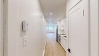 Located at 5205-5215 1re Ave in Montréal, this efficiently designed single-floor unit offers a thoughtful layout that maximizes its compact footprint. The space is arranged as a long, narrow floor plan, seamlessly connecting the kitchen and living area in one continuous flow.

The galley-style kitchen is well-appointed with crisp white shaker cabinetry extending from floor to ceiling, stainless steel appliances including a full-size refrigerator and oven, a single-basin sink, and recessed pot lighting overhead. The clean white walls and light wood-look flooring create a bright, cohesive aesthetic throughout.

The living area is open and airy, benefiting from recessed lighting and large windows that invite natural light deep into the space. A door with a glass panel provides direct access to an outdoor balcony, offering views of lush greenery and the surrounding neighbourhood — a standout feature that brings the outdoors in. A baseboard heating system runs along the exterior wall beneath the windows, ensuring year-round comfort.

The consistent light wood flooring and crisp white walls throughout the unit create a clean, modern ambiance. The space is practical and well-finished, making it an efficient and inviting urban dwelling in the heart of Montréal.