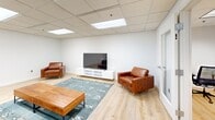 Located at 601 Penn St in Reading, PA, this single-floor space offers a well-designed layout that balances productivity and recreation. The interior is finished with clean white walls, light wood-style flooring, and a drop ceiling with integrated panel lighting, creating a bright and welcoming atmosphere throughout.

The main open area serves as a versatile lounge and recreation hub. It features a full-size pool table as a central focal point, accompanied by multiple seating arrangements including a tufted gray sofa, two cognac leather armchairs, a solid wood coffee table, and a patterned area rug. A flat-screen TV mounted on a sleek white media console adds an entertainment component, while round white dining tables with modern chairs provide space for casual meetings or collaborative work. The open layout allows for easy flow between the lounge, dining, and game areas.

A separate private room provides a focused workspace, outfitted with a glass-top desk and an ergonomic office chair — ideal for individual work or small meetings requiring privacy.

Throughout the space, the consistent design language of neutral tones, modern furnishings, and clean finishes contributes to a professional yet comfortable environment suited for coworking, team gatherings, or community use.