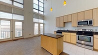 Located at 4437 Glengarry Dr in Beavercreek, Ohio, this two-story residence offers a striking open-concept layout defined by soaring double-height ceilings and expansive floor-to-ceiling windows that flood the main living area with natural light. French doors lead to a private balcony, extending the sense of openness and providing outdoor views. The kitchen is well-appointed with light maple cabinetry, dark granite countertops, a central island, stainless steel appliances including a range, microwave, and dishwasher, and tile flooring that transitions into plush carpeting throughout the living areas. Pendant lighting adds a modern touch above the kitchen island. The upper level features carpeted bedrooms, including one with a double-door closet and an adjacent en-suite bathroom equipped with a glass-enclosed shower stall and tile flooring. A second full bathroom on the lower level includes a soaking tub and shower combination, also finished with tile floors. Additional bedrooms offer bright windows and soft neutral tones throughout. The overall ambiance is clean, modern, and bright, with an emphasis on open space, practical storage, and comfortable living across both floors.