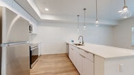 Located at The Oasis in West Sacramento, CA, this two-bedroom, one-bathroom residence offers a thoughtfully designed single-floor layout with a bright, modern aesthetic. Light wood plank flooring flows seamlessly throughout the entire space, creating a cohesive and airy feel.

The open-concept kitchen serves as the centerpiece of the home, featuring sleek flat-front white cabinetry, light quartz countertops, and a large peninsula with an undermount sink — ideal for both cooking and casual dining. Stainless steel appliances, including a range, microwave, and dishwasher, complement the clean design. A trio of globe pendant lights with brass accents hang above the peninsula, adding a contemporary touch. Recessed lighting and a tray ceiling detail further elevate the space.

The primary bedroom offers a comfortable footprint with a built-in closet featuring wire shelving and direct sightlines to the kitchen area, enhancing the open flow. The second bedroom benefits from a large window that brings in natural light and views of the surrounding neighborhood.

The bathroom is finished with a wide vanity topped in white quartz, flat-front cabinetry below, and a large mirror, maintaining the home's clean, modern palette. Crisp white walls throughout keep the space feeling fresh and versatile.