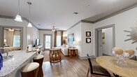 Located at 4211 Commons Dr W in Destin, FL, this thoughtfully designed 2-bedroom, 2-bathroom model suite offers a comfortable single-story layout with a warm coastal aesthetic throughout. The open-concept living and dining area is anchored by wood-look flooring, crown molding, and a ceiling fan, with natural light streaming in through large windows dressed in textured drapes. The living room features generous proportions ideal for relaxed coastal living. The combined kitchen and dining area showcases rich dark cabinetry, granite-style countertops, stainless steel appliances, and a pantry for added storage. Both bathrooms are well-appointed with tub/shower combinations, wood-tone vanities, and tile accents. The spacious primary bedroom includes plush carpeting, a ceiling fan, and ample natural light, while the second bedroom offers similar comfort. Four closets provide excellent storage throughout. Additional highlights include a dedicated laundry area, a hallway connecting the private spaces, and a patio for outdoor enjoyment. The overall ambiance reflects a relaxed, beach-inspired sensibility that complements the Destin, Florida setting beautifully.