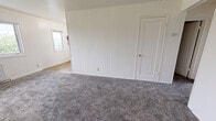 Located at 787 Elm St in Anchorage, Alaska, this single-floor unit offers three bedrooms and one bathroom with a straightforward, functional layout. The interior is finished in a clean, neutral palette throughout, with white walls and ceilings that maximize brightness.

The generously sized primary bedroom features distinctive white vertical shiplap wall paneling, plush grey carpet, and multiple windows that allow natural light to filter in. Radiator heating units are present in the bedrooms, providing reliable warmth suited to Alaska's climate. The two additional bedrooms are more compact but equally well-lit, each with carpeted flooring, windows with exterior views, and radiator heating. One secondary bedroom includes a sliding closet door for added storage.

The bathroom is clean and efficiently appointed, featuring a full tub-shower combo with chrome fixtures, a wall-mounted sink, and a mirrored medicine cabinet above, set on tile flooring.

Common areas transition between tile flooring near the entry and carpeted living spaces. The kitchen, visible in the dollhouse view, includes a white electric range and cabinetry. A hallway connects the main living spaces. The unit is equipped with a fire extinguisher for safety. Overall, the space presents a practical and comfortable living environment in a central Anchorage location.