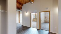 Located at 550 W Western Ave in Muskegon, MI, this two-bedroom, one-bathroom loft blends industrial character with contemporary updates across a single thoughtfully laid-out floor. Soaring ceilings with warm, exposed wood beams and visible ductwork establish a distinctive loft aesthetic throughout the common areas and hallways. Dark wood-look flooring runs through the living and kitchen areas, while plush carpet adds comfort to the bedrooms.

The open kitchen is equipped with stainless steel appliances, including a refrigerator, range, and over-the-range microwave, complemented by modern flat-front cabinetry and light countertops. A peninsula with a sink opens toward the living area, enhancing the space's open feel. Structural wood posts punctuate the living area, reinforcing the building's original industrial character.

Both bedrooms offer carpeted floors and generous ceiling height, with the primary bedroom showcasing exposed brick accent walls and tall, wood-framed windows that flood the room with natural light. The full bathroom features a tub-shower combination, a single-sink vanity with modern cabinetry, and wood-look tile flooring. Two hallways connect the rooms efficiently, and a dedicated closet provides additional storage. The overall ambiance balances raw, historic architectural elements with clean, modern finishes.