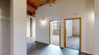 Located at 550 W Western Ave in Muskegon, MI, this two-bedroom, one-bathroom loft blends industrial character with contemporary updates across a single thoughtfully laid-out floor. Soaring ceilings with warm, exposed wood beams and visible ductwork establish a distinctive loft aesthetic throughout the common areas and hallways. Dark wood-look flooring runs through the living and kitchen areas, while plush carpet adds comfort to the bedrooms.

The open kitchen is equipped with stainless steel appliances, including a refrigerator, range, and over-the-range microwave, complemented by modern flat-front cabinetry and light countertops. A peninsula with a sink opens toward the living area, enhancing the space's open feel. Structural wood posts punctuate the living area, reinforcing the building's original industrial character.

Both bedrooms offer carpeted floors and generous ceiling height, with the primary bedroom showcasing exposed brick accent walls and tall, wood-framed windows that flood the room with natural light. The full bathroom features a tub-shower combination, a single-sink vanity with modern cabinetry, and wood-look tile flooring. Two hallways connect the rooms efficiently, and a dedicated closet provides additional storage. The overall ambiance balances raw, historic architectural elements with clean, modern finishes.