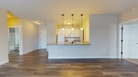 Located at 38401 Mentor Ave in Willoughby, Ohio, this single-floor residence offers a well-designed layout with a cohesive blend of modern finishes and practical living spaces. The open-concept living and kitchen area serves as the heart of the home, where rich hardwood-style flooring extends throughout. The kitchen features white cabinetry, granite countertops, white appliances including a refrigerator, range, and built-in microwave, and a peninsula breakfast bar illuminated by three pendant lights — creating a functional and inviting space. The living area is generously sized, with a large sliding glass door and adjacent window that allow abundant natural light to fill the room. The bedrooms are carpeted for comfort, with multiple windows providing natural light; one bedroom includes a ceiling fan overhead. Two full bathrooms serve the unit — one with a glass-enclosed walk-in shower and wood-look flooring, and another with a full soaking tub and shower combination, both finished with white vanities and neutral countertops. Additional utility space, including an electrical panel closet, is accessible from the kitchen corridor. The overall palette of warm neutrals and clean white trim creates a bright, move-in-ready atmosphere throughout.