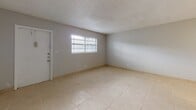 This renovated one-bedroom, one-bathroom unit at Azure Villas in Pembroke Park, Florida offers a clean, move-in-ready layout spread across a single floor. Light-toned tile flooring runs consistently throughout the space, contributing to a bright and cohesive aesthetic. The living area is open and well-proportioned, featuring neutral gray walls, a textured ceiling, and a window with blinds that allows natural light to fill the room. The entry door is fitted with a secure deadbolt lock for added peace of mind. The kitchen has been thoughtfully updated with crisp white shaker-style cabinetry, a neutral countertop with a tile backsplash, and a full suite of black appliances including a refrigerator, electric range, dishwasher, and built-in microwave. A flush-mount ceiling fixture provides overhead lighting, and an HVAC vent ensures climate comfort. The bedroom is a comfortable, well-lit room with a window, a built-in closet with louvered doors, and a programmable thermostat nearby. The bathroom features a white vanity with a framed mirror, brushed nickel fixtures, a combined tub and shower, and matching tile flooring that ties the space together. Overall, the unit presents a clean, functional, and updated living environment.