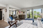 This well-designed single-floor home offers three bedrooms and one bathroom across a thoughtfully laid-out floor plan. The bright and open living room serves as the heart of the home, featuring durable hardwood-style flooring, a textured ceiling, and large sliding glass doors that flood the space with natural light and provide direct access to an outdoor balcony with pleasant greenery views. The galley-style kitchen is a functional standout, boasting rich dark wood cabinetry, granite-look countertops, and a full suite of black appliances including a gas range, dishwasher, and refrigerator, all complemented by light wood-style flooring. The primary bedroom is generously proportioned with plush carpet, ample natural light from well-dressed windows, and direct access to the shared bathroom. The bathroom features a dark wood vanity with a clean countertop and a tiled tub-shower combination. Additional bedrooms offer comfortable carpeted spaces with room for varied uses. A hallway with wood-style flooring connects the rooms efficiently. The primary bedroom also benefits from a spacious walk-in closet with built-in shelving rods, providing excellent storage throughout this well-appointed home.