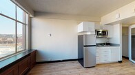Located on the eighth floor at 515 West Sprague Avenue in downtown Spokane, Washington, this single-floor studio unit offers a practical and efficiently designed living space. The open-concept layout seamlessly combines the living and kitchen areas, finished with light wood-tone luxury vinyl plank flooring throughout and a textured ceiling that adds character to the space.

The kitchenette is well-appointed with white cabinetry, a gray countertop, a stainless steel refrigerator, a two-burner electric cooktop, a sink, and an over-the-range stainless steel microwave — providing all essential cooking amenities in a compact footprint. A large picture window along one wall fills the main living area with natural light while framing views of the downtown Spokane skyline. Beneath the window sits a built-in wood-paneled bench, adding both storage and a cozy architectural detail.

The bathroom features a granite-style countertop with an undermount sink, white subway tile accents, a mirrored medicine cabinet, and a full tub and shower. A separate walk-in closet with a rod and shelving is accessible directly from the bathroom area, offering ample storage. The sleeping area is defined by clean white walls and continued plank flooring, providing a calm and versatile space. A mirrored door adds depth and light to the unit's interior.