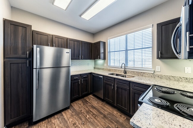 Kitchen with espresso cabinetry, speckled granite countertops, white subway tile backsplash, stainless steel appliances, and hard surface flooring - eaves North Dallas