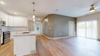 Located at 6386 Transit Rd in Lancaster, NY, this single-floor residence offers a thoughtfully designed open-concept layout with modern finishes throughout. The kitchen serves as a central highlight, featuring crisp white shaker cabinetry, granite countertops, a classic subway tile backsplash, stainless steel appliances, and a large center island with a deep undermount sink and pendant lighting. The kitchen flows seamlessly into the living and dining areas, which are finished with light hardwood flooring and accented by warm greige walls that lend a contemporary, neutral aesthetic. Large sliding glass doors and multiple windows in the living area invite abundant natural light and provide outdoor views. The bedrooms are carpeted for comfort, with ceiling fans and windows that bring in additional natural light. A full bathroom includes a soaking tub with a tub-surround enclosure and brushed nickel fixtures. Throughout the unit, clean white trim, recessed lighting, and consistent flooring choices create a cohesive and polished look. The single-floor plan ensures easy accessibility and a practical flow between all living spaces, making this a well-appointed and move-in-ready residence.
