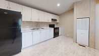 Located at 2214 E Fourth Ave in Hutchinson, Kansas, this single-story, two-bedroom, one-bathroom home offers a compact yet efficiently organized layout across its single floor. The elongated floor plan, visible in the 3D overview, arranges all rooms along a central corridor, maximizing usability throughout the space.

The kitchen is equipped with white shaker-style cabinetry extending from base to upper wall, light-toned countertops, a double-basin sink, a black electric range, and a refrigerator. Recessed lighting and light wood-look flooring contribute to a clean, functional cooking environment.

The primary bedroom is notably spacious, featuring vaulted ceilings, neutral textured wall panels, light wood-look flooring, and a window with blinds that admits natural light. An adjoining bathroom is directly accessible from this room. The second bedroom is similarly appointed with matching flooring, textured walls, vaulted ceilings, a window, and a wall-mounted clothing rod for storage.

The bathroom includes a full tub-shower combination with a handheld showerhead, tile-look wall surround, a toilet, and a vanity with white cabinetry. The hallway area features a built-in HVAC unit, providing centralized climate control. Consistent light flooring and neutral wall tones throughout create a cohesive, understated ambiance.