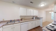 This single-story unit at The Brickyard offers a thoughtfully arranged layout with a clean, neutral aesthetic throughout. The kitchen serves as a functional centerpiece, featuring an expansive run of white cabinetry — both upper and lower — paired with laminate countertops that provide ample workspace. White appliances, including a full-size refrigerator, dishwasher, and range, are seamlessly integrated into the design. Dark hardwood-style flooring runs through the kitchen, adding warmth and contrast to the bright cabinetry. A window above the sink area allows natural light to filter in.

The living area transitions to plush carpeting and is highlighted by a ceiling fan and a large sliding glass door fitted with vertical blinds, offering views of lush outdoor greenery and providing access to the exterior. An adjacent window further enhances natural light in the space.

The bedrooms are generously sized, each finished with soft carpeting, ceiling fans with light fixtures, and windows that bring in natural daylight. Closet storage is included in the bedroom areas.

The bathroom features a white vanity with a large mirror, well-lit by a Hollywood-style light bar above. Dark hardwood-style flooring continues here, complementing the clean white fixtures and a shower-tub combination.