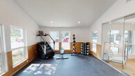 Located at 8401 Skillman St in Dallas, Texas, this fitness center offers a well-appointed, single-floor workout facility designed with both functionality and aesthetics in mind. The space features soaring vaulted ceilings that lend an open, airy atmosphere throughout, complemented by crisp white walls and warm wood wainscoting that runs along the lower portion of each wall, adding a refined architectural detail to the interior.

Natural light pours in generously through multiple windows positioned around the perimeter, illuminating the durable rubber flooring that covers the workout area. The fitness floor is divided into distinct zones to accommodate a variety of training styles. A dedicated cardio section houses elliptical trainers, a stair climber, and a stationary spin bike, all positioned to take advantage of the natural light and outdoor views. Framed artwork adorns the walls, adding a polished, welcoming touch to the cardio zone.

A well-stocked free weights area features a full rack of dumbbells, a medicine ball tower, and a kettlebell rack, providing ample options for strength training. The space is connected to an adjacent area via full-height sliding glass doors, which allow for an open flow between zones while maintaining visual separation. Recessed lighting throughout ensures the space remains well-lit at all hours, making this fitness center a comprehensive and inviting environment for exercise.