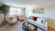 This single-floor residence offers a thoughtfully arranged layout that maximizes both comfort and functionality. The living room serves as the central gathering space, featuring plush carpeting, neutral wall tones, and large windows that invite natural light while providing outdoor views. A baseboard heating system runs along the perimeter, and the room accommodates multiple seating arrangements with ease.

Adjacent to the living area, the dining space is anchored by an elegant chandelier overhead and offers enough room for a round dining table with seating for four. Carpet flooring continues throughout, contributing to a cohesive, warm aesthetic. A console area nearby provides additional utility.

The kitchen is efficiently designed with warm wood cabinetry, laminate countertops, a stainless steel sink, and white appliances including a gas range and dishwasher. Tile flooring and under-cabinet lighting enhance the practical workspace.

The bedroom is generously proportioned, featuring carpet flooring, a closet with double doors, and windows that frame outdoor scenery. The bathroom includes a wood-toned vanity with white countertop, a medicine cabinet mirror, and clean, bright finishes throughout.