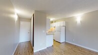 This single-floor, 2-bedroom, 1-bathroom unit offers a practical and well-organized layout. The living room is the largest shared space, featuring wood-style plank flooring, neutral-toned walls, and a textured ceiling. A sliding glass door at the far end fills the room with natural light and provides access to a private balcony with outdoor views, enhancing the sense of openness.

The galley-style kitchen runs along a narrow corridor and is efficiently designed with white upper and lower cabinetry, gray laminate countertops, a stainless single-basin sink, and white appliances including a range and full-size refrigerator. A window above the counter brings in additional natural light.

Both bedrooms feature carpet flooring, neutral walls, and windows with horizontal blinds overlooking greenery. The primary bedroom includes a sliding-door closet with a built-in shelf. A hallway connects the bedrooms to the shared full bathroom, which includes a tub-shower combination, a white vanity with gray countertop, and wood-style flooring consistent with the rest of the unit's common areas.