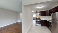 This single-floor residence at Jumping Brook offers a well-designed layout with a consistent blend of functionality and comfort throughout. The kitchen is a standout feature, equipped with a full suite of stainless steel appliances including a gas range, built-in microwave, dishwasher, and refrigerator. Rich dark-toned cabinetry extends to the ceiling, providing generous storage, while light-colored countertops and light tile flooring create a clean, contemporary contrast.

The living area is generously proportioned, featuring warm hardwood flooring that continues throughout the main living spaces and bedrooms. A sliding glass door floods the room with natural light and provides direct access to a private balcony with outdoor views. A wall-mounted air conditioning unit and baseboard heating ensure year-round comfort.

The bedrooms are well-sized, with hardwood floors and neutral walls. One bedroom notably features dual sliding closets, offering exceptional storage capacity, while a second bedroom includes a single closet and a bright window with a baseboard heater beneath it.

The bathroom is finished in clean white tiling with a textured accent wall, a soaking tub with shower, and dark slate-style floor tiles, lending a crisp, modern feel to the space.