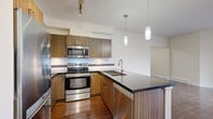 This thoughtfully designed one-bedroom, one-bathroom residence offers a comfortable and functional layout across a single floor. The open-concept kitchen is a standout feature, showcasing rich wood-grain cabinetry, dark granite countertops, a peninsula island with an undermount sink, and a full suite of stainless steel appliances including a range, built-in microwave, dishwasher, and refrigerator. Pendant lighting and a ceiling-mounted track light illuminate the space, while a mosaic tile backsplash adds a refined detail. Rich hardwood flooring extends through the kitchen and living areas, lending warmth throughout. The living room is bright and airy, benefiting from a sliding glass door that opens to an outdoor area, allowing natural light to flow freely into the space. The bedroom features plush carpet flooring and a window with an exterior view, creating a calm and restful atmosphere. The bathroom is finished with large-format tile flooring, a wood-grain vanity with granite countertop, and a well-lit mirror. A dedicated laundry area houses a stacked washer and dryer unit. A closet provides additional storage, completing this efficiently organized and modern residence.