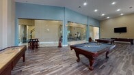 Located at 429 Valley St in Providence, Rhode Island, this single-floor amenity complex offers an impressive array of shared spaces designed for comfort, recreation, and convenience. The welcoming lobby greets visitors with large-format tile flooring, glass-panel walls, and floor-to-ceiling windows that draw in abundant natural light. A modern communal kitchen features granite countertops, white shaker-style cabinetry, stainless steel appliances, and a peninsula with seating — ideal for casual gatherings. A dedicated dining area with multi-pane windows and rich hardwood-style flooring provides a warm, functional setting for shared meals. The lounge area is anchored by a dramatic stone accent wall with a fireplace and mounted television, complemented by tall windows and plush seating. The recreation amenities are extensive: a full indoor basketball court with a regulation hoop and branded court surface connects directly to a glass-enclosed fitness center equipped with exercise machines. A billiards room with hardwood flooring and high ceilings rounds out the leisure offerings. The expansive covered parking garage features soaring vaulted ceilings, concrete flooring, yellow safety bollards, and dedicated bicycle storage — providing ample, well-organized vehicle and bike accommodation for residents.