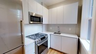 This 2-bedroom, 1-bathroom single-floor residence showcases a thoughtfully designed interior with a clean, contemporary aesthetic. The kitchen stands out as a highlight of the space, outfitted with stainless steel appliances including a gas range with oven, a built-in Bosch microwave, and a refrigerator. Flat-front white cabinetry extends floor-to-ceiling, maximizing storage while contributing to a crisp, minimalist look. White quartz-style countertops run along the L-shaped layout, providing ample prep space, and a stainless steel undermount sink with a modern arc-neck faucet adds a functional, polished touch. A seamless white backsplash ties the kitchen together with a cohesive, streamlined appearance. Light hardwood flooring runs throughout, adding warmth and continuity to the space. The overall design reflects a modern sensibility with neutral tones, quality finishes, and efficient use of space, making it well-suited for everyday living.