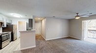Located at 317 Lynn Rd in Raleigh, NC, this single-floor residence offers a well-organized layout with a neutral color palette and a mix of carpet and wood-look flooring throughout. The open living area is bright and spacious, anchored by plush carpeting and a peninsula countertop that connects seamlessly to the kitchen, making the space feel cohesive and functional. The galley-style kitchen is efficiently designed with gray cabinetry, granite-look countertops, stainless steel appliances including a refrigerator and dishwasher, and a double sink — all finished with light wood-look flooring. The bedrooms are generously sized, each featuring carpet flooring, ceiling fans with light fixtures, and ample natural light from windows with blinds. The primary bedroom includes access to a dedicated bathroom and a walk-in closet. Both bathrooms are finished with wood-look flooring, gray vanity cabinetry, white countertops, and large mirrors. The full bath features a tub-shower combination with tile surround. A dedicated laundry area houses a full-size washer with overhead wire shelving, providing added convenience. Textured ceilings are consistent throughout, adding a classic finishing touch to the overall interior.