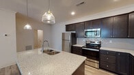This single-floor residence in Lexington, Kentucky, offers a thoughtfully designed open-concept layout with consistent finishes throughout. Light wood-style flooring extends across the main living areas, complementing the neutral white walls and crown molding details that contribute to a clean, contemporary aesthetic.

The kitchen serves as a central focal point, anchored by a large island with a double undermount sink, granite countertops, and seeded glass pendant lighting overhead. Rich, dark-stained cabinetry with shaker-style doors provides ample storage, while a textured tile backsplash adds visual interest. Stainless steel appliances, including a refrigerator, electric range, and built-in microwave, complete the space.

The living area is open and bright, featuring a ceiling fan and glass door that leads to an outdoor balcony, allowing natural light to flow in. Bedrooms feature light-toned wood flooring, neutral walls, and windows with blinds. A walk-in closet is accessible from one of the bedroom areas.

The bathroom is finished with tile flooring, a soaking tub and shower combination, a dark-stained vanity with granite countertops, and a large mirror. Throughout the residence, consistent materials and finishes create a cohesive and modern atmosphere.