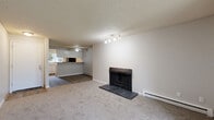 Located in Everett, WA, this single-floor, 3-bedroom, 2-bathroom home offers a practical and comfortable layout. The living room serves as the heart of the space, anchored by a wood-burning brick fireplace and finished with plush carpet, a textured ceiling, and a track lighting fixture. Baseboard heating runs throughout. A ceiling fan bridges the living area to the kitchen, which features a galley-style design with wood-look flooring, white cabinetry, light countertops, and black appliances including a refrigerator, electric range, dishwasher, and an overhead range hood. A pass-through counter connects the kitchen to the main living area. A separate room with a sliding glass door provides direct access to an outdoor green space, bringing in natural light and outdoor views. The three bedrooms are carpeted and feature textured ceilings, neutral walls, and sliding-door closets. The primary bedroom includes a window overlooking lush greenery and a baseboard heater. Both bathrooms share a consistent design with wood-look flooring, white vanities, and a tub-shower combination with warm-toned surround walls. Two hallways connect the rooms efficiently throughout the home.