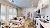 Located in Conroe, TX, this thoughtfully designed single-floor unit maximizes its compact footprint with an efficient, open-concept layout. Light wood flooring runs throughout, lending warmth and visual continuity across every room.

The living area is bright and welcoming, anchored by large windows that draw in abundant natural light and offer outdoor views. A ceiling fan adds comfort, while the open layout connects seamlessly to the dining area and kitchen.

The kitchen is well-appointed with tall white shaker cabinets reaching toward the ceiling, a subway tile backsplash, stainless steel appliances including a refrigerator, range, over-the-range microwave, and dishwasher, and a clean white countertop with a functional sink — all designed to make the most of the available space.

A hallway lined with recessed lighting connects the main living areas to the private spaces, including a cozy bedroom with neutral tones and ample closet storage across three dedicated closets. The two bathrooms are cleanly finished, one featuring a walk-in shower with a black-framed glass door and white tile surround.

A dedicated laundry area adds everyday convenience. The overall ambiance is modern yet warm, with a neutral palette and recessed lighting creating a comfortable, inviting atmosphere throughout.