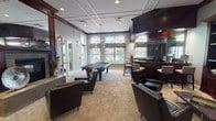 Located at 1555 Mesa Ln in Aurora, Illinois, this sophisticated single-story clubhouse offers a series of thoughtfully designed communal spaces that blend classic architectural detail with upscale amenities. The grand entrance lobby sets an impressive tone with soaring ceilings, rich hardwood flooring in a herringbone pattern, and stately columns flanking a set of arched, floor-to-ceiling windows that flood the space with natural light and frame views of the outdoor pool area. Elegant drapery and plush seating arrangements create a welcoming, refined atmosphere throughout.

The main lounge area features a striking gas fireplace with a rich mahogany surround and an oversized mirror above the mantle, complemented by tufted leather armchairs and a coffered ceiling with recessed lighting. Adjacent to the lounge, a dedicated billiards room offers a full-size pool table, leather seating, and a wet bar with dark granite countertops and bar-height seating — ideal for social gatherings. A media lounge nearby includes a built-in mahogany entertainment center with flat-screen television, additional club seating, and a coffered ceiling that maintains the space's consistent design language. Throughout, neutral tones, dark wood accents, and carefully curated décor contribute to a cohesive, club-like ambiance.