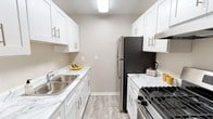 This single-floor residence offers a thoughtfully designed layout that balances comfort and functionality. The galley-style kitchen stands out as a highlight of the unit, showcasing white shaker cabinetry with brushed nickel hardware, marble-look countertops, light wood-look vinyl flooring, and stainless steel appliances including a gas range and refrigerator — all illuminated by flush ceiling lighting.

The living area is generously sized, featuring plush wall-to-wall carpeting, a ceiling fan, and a vertical-blind-covered sliding glass door that opens to a private balcony, inviting natural light into the space. A distinctive vertical panel accent wall adds a touch of character to the room. An open flow connects the living space to additional areas of the unit.

The bedroom is a comfortable, carpeted retreat with neutral-toned walls, a baseboard heating unit, and a window fitted with blinds that allow for adjustable natural light.

The full bathroom is clean and functional, featuring a white vanity with an integrated sink, a tub-shower combination with white tile surround, wood-look vinyl flooring, a mirrored medicine cabinet, and a baseboard heater. The overall aesthetic throughout the unit is fresh and neutral, with a consistent warm-gray and white palette that creates a bright, move-in-ready atmosphere.