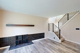 Located at 1997 Villa Rd in Birmingham, MI, this thoughtfully updated multi-level home spans three floors and offers a clean, modern aesthetic throughout. The main living area centers around a bold black brick fireplace with a dark wood mantel and frosted glass cabinet doors, complemented by light hardwood-style flooring and a sleek black metal staircase railing that adds a contemporary industrial touch. Large sliding glass doors flood the living room with natural light and provide access to the outdoors. The kitchen is well-appointed with white shaker cabinetry, dark granite countertops, stainless steel appliances, and a peninsula with decorative columns — opening seamlessly to the dining area. The two bedrooms are carpeted for comfort; the second bedroom features built-in shelving along an entire wall, ideal for storage or display, while the primary bedroom includes a stylish frosted-glass sliding door. The shared bathroom is elegantly finished with a double granite vanity, matte black fixtures, a framed mirror, and white subway tile in the shower surround. The basement level offers an open, unfinished space with white-painted walls and a utility sink, presenting flexible potential. Three stairwells and multiple closets provide excellent connectivity and storage throughout.