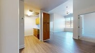 This 2-bedroom, 1-bathroom single-floor unit offers a practical and well-designed layout that maximizes functionality throughout. The open-concept living area is bright and airy, featuring light-toned luxury vinyl plank flooring and a ceiling fan with a pendant light fixture. A large window floods the space with natural light and provides views of the surrounding exterior, enhancing the overall sense of openness. The kitchen is positioned adjacent to the living area and features warm wood-toned cabinetry, a stainless steel refrigerator, an electric range, a dishwasher, and a tall storage pantry cabinet — offering ample storage and a complete set of appliances. The primary bedroom is generously sized and finished with light hardwood-style flooring and large windows that invite abundant natural light. The secondary bedroom features soft carpeting and a vertical window with blinds for privacy. Three closets throughout the unit provide excellent storage capacity. The bathroom is clean and functional, equipped with a walk-in shower featuring grab bars and a handheld showerhead, wood-toned vanity cabinetry, and matching vinyl plank flooring. Neutral wall tones and consistent flooring throughout create a cohesive and move-in ready environment.