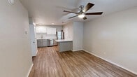 Located at 7806 SW Blue Jay Ln in Bentonville, Arkansas, this efficient one-bedroom, one-bathroom home offers a thoughtfully designed single-floor layout. Wood-look flooring flows consistently throughout the entire space, lending warmth and visual continuity from room to room.

The combined kitchen and living area forms the heart of the home. The living room features neutral beige walls, a ceiling fan with integrated lighting, and a front entry door with an arched transom window that welcomes natural light. A second window provides additional brightness and outdoor views.

The kitchen is well-appointed with white upper cabinetry, gray lower cabinets, and crisp white quartz countertops. A classic white subway tile backsplash adds a clean, modern touch. Stainless steel appliances — including a refrigerator, dishwasher, electric range, and over-the-range microwave — complete the functional cooking space. A breakfast bar peninsula connects the kitchen to the living area.

The bedroom is a comfortable, well-proportioned retreat with neutral walls, a ceiling fan, a window with blinds, and access to a dedicated closet. The bathroom features a gray vanity with a white countertop, a lighted mirror, a full soaking tub with shower, and consistent wood-look flooring that ties the space together with the rest of the home.