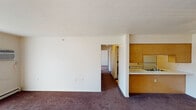 Located at 1080 S Peru St in Cicero, Indiana, this single-floor unit offers a straightforward, functional layout distributed across several interconnected rooms. The living area is finished with dark wall-to-wall carpeting and neutral white walls, and features a full-width sliding glass door dressed with vertical blinds, allowing natural light to filter in while providing a direct view of the surrounding greenery. A wall-mounted air conditioning unit and baseboard heating serve the space.

The galley-style kitchen runs along two parallel walls and is well-equipped with white cabinetry trimmed in warm wood accents, white appliances including a range, refrigerator, and dishwasher, a double stainless steel sink, and light vinyl tile flooring. A pass-through connects the kitchen to the main living area.

The bedrooms are carpeted and each features bi-fold closet doors with rod and shelf storage. One bedroom includes a ceiling fan with light fixture, while the other benefits from a window that admits natural light. Baseboard heaters are present throughout.

The bathroom offers tile flooring, a long vanity with a single sink and ample counter space, a wall mirror, and accessibility-friendly grab bars positioned near the toilet. The textured ceilings are consistent throughout the unit, contributing to its clean, utilitarian character.