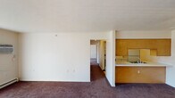 Located at 1080 S Peru St in Cicero, Indiana, this single-floor unit offers a straightforward, functional layout distributed across several interconnected rooms. The living area is finished with dark wall-to-wall carpeting and neutral white walls, and features a full-width sliding glass door dressed with vertical blinds, allowing natural light to filter in while providing a direct view of the surrounding greenery. A wall-mounted air conditioning unit and baseboard heating serve the space.

The galley-style kitchen runs along two parallel walls and is well-equipped with white cabinetry trimmed in warm wood accents, white appliances including a range, refrigerator, and dishwasher, a double stainless steel sink, and light vinyl tile flooring. A pass-through connects the kitchen to the main living area.

The bedrooms are carpeted and each features bi-fold closet doors with rod and shelf storage. One bedroom includes a ceiling fan with light fixture, while the other benefits from a window that admits natural light. Baseboard heaters are present throughout.

The bathroom offers tile flooring, a long vanity with a single sink and ample counter space, a wall mirror, and accessibility-friendly grab bars positioned near the toilet. The textured ceilings are consistent throughout the unit, contributing to its clean, utilitarian character.