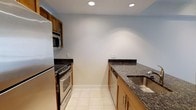 Unit Astoria 1101 is a thoughtfully designed 1-bedroom, 1-bathroom residence spread across a single floor. The unit offers a comfortable and efficient layout well-suited for everyday living.

The kitchen is a standout feature, showcasing warm wood cabinetry paired with rich dark granite countertops that provide ample prep and storage space. Stainless steel appliances — including a gas range with oven, built-in microwave, refrigerator, and dishwasher — lend a modern, functional edge to the space. A deep stainless steel sink with a contemporary faucet completes the setup. The kitchen is finished with clean white tile flooring and recessed lighting overhead, creating a bright and practical cooking environment.

The galley-style kitchen layout maximizes efficiency, with cabinetry and appliances lining both sides to make the most of the available space. Neutral wall tones throughout contribute to a clean, versatile aesthetic that complements a variety of décor styles.

Overall, Unit Astoria 1101 presents a well-maintained, move-in-ready residence with a cohesive design that balances practicality and comfort — an ideal option for those seeking a streamlined, single-floor living experience.