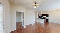 This single-story, 1-bedroom, 1-bathroom unit in Baton Rouge, Louisiana is designed with a functional and open layout. Rich hardwood-style flooring runs throughout the entire space, lending warmth and consistency from room to room. The living area is generously sized, featuring a ceiling fan with light fixture, multiple windows that invite natural light, and a glass-paneled front door that enhances the bright, airy ambiance. The open-concept design connects the living area directly to the kitchen, which is outfitted with dark espresso cabinetry, black appliances including a refrigerator and electric range, a double basin sink, and a breakfast bar peninsula for casual dining. A decorative chandelier adds a touch of elegance to the dining area adjacent to the kitchen. The bedroom is well-proportioned, featuring a ceiling fan, windows with blinds, and direct access to the full bathroom. The bathroom includes a dark vanity with a single sink, a soaking tub, and a mirrored medicine cabinet. A dedicated laundry closet with washer/dryer hookups and a wire shelf provides additional utility. The unit's neutral color palette and clean architectural lines create a versatile and move-in-ready living environment.