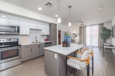 Located at 950 E 3rd St in Los Angeles' vibrant Arts District, this one-bedroom, one-bathroom residence offers a thoughtfully designed single-floor layout with a clean, contemporary aesthetic throughout. The open-concept kitchen is a standout feature, showcasing two-tone gray and white cabinetry, a geometric tile backsplash, stainless steel appliances including a refrigerator, range, microwave, and dishwasher, and a central island with pendant lighting and bar seating — ideal for both cooking and casual dining. Light wood-style flooring flows through the kitchen and living areas, enhancing the bright, airy feel of the space. The living room is generously proportioned with large floor-to-ceiling windows dressed in neutral drape panels that invite abundant natural light and city views. A ceiling fan adds a practical touch. The bedroom offers plush carpeting, a textured accent wall, a ceiling fan, and large windows that continue the theme of natural light. A dedicated closet provides ample storage. The full bathroom features subway tile surrounding the soaking tub and shower, a white vanity with a wide mirror, and tile flooring. Additional spaces include a pantry, hallway, laundry area, and closet, rounding out a highly functional and stylish urban residence.