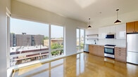 This thoughtfully designed single-floor unit blends contemporary architecture with functional living. The open-concept main living area is anchored by gleaming polished concrete floors that reflect abundant natural light pouring in through expansive floor-to-ceiling windows. These large windows frame elevated views of the surrounding urban streetscape, creating a bright and airy atmosphere throughout.

The kitchen is seamlessly integrated into the living space and features a clean, modern aesthetic with two-tone cabinetry — warm wood-grain lower cabinets paired with white upper cabinets and open shelving. A white subway tile backsplash, stainless steel appliances including a gas range, dishwasher, and refrigerator, and a matte black faucet over an undermount sink complete the well-appointed culinary space. A stylish pendant light overhead adds a warm design accent.

The bedroom is a calm, light-filled retreat with polished concrete floors continuing from the main space, a wall-mounted split HVAC unit for individual climate control, and a window with urban views. The room is equipped with a sliding-door closet offering generous built-in storage.

The bathroom maintains the unit's clean, minimalist design language with a floating white vanity, an undermount sink, matte black fixtures, a mirrored medicine cabinet, and a globe pendant light. Throughout, crisp white walls and purposeful finishes create a cohesive, modern living environment.