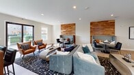 The Club Room at 321 S Broad St in Elizabeth, NJ is a thoughtfully designed communal space that seamlessly blends comfort and functionality. The open-concept layout is anchored by a welcoming lounge area furnished with plush seating, including a soft blue sectional sofa and rich cognac leather armchairs, all set atop a bold patterned area rug. Warm wood accent walls serve as striking design elements, framing cozy booth-style nooks that are ideal for small gatherings or focused work sessions. Natural light pours in through multiple windows fitted with classic white blinds, creating a bright and inviting atmosphere throughout. The kitchen area is well-appointed with rich, dark cabinetry, granite countertops, a white subway tile backsplash, and full-size stainless steel appliances including a refrigerator with water dispenser and a microwave. A dedicated coffee bar adds a convenient amenity for residents. Light-toned tile flooring runs throughout the space, lending a clean and cohesive aesthetic. A set of black-framed glass doors opens directly to an outdoor terrace, extending the space and providing a refreshing connection to the outdoors. The Club Room offers a polished, community-centered environment designed to encourage both relaxation and social interaction.