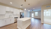 Located at 1023 Gull Ln in Melbourne, FL, this well-designed one-bedroom, one-bathroom unit offers a thoughtful layout across a single floor. The open-concept kitchen, dining, and living area forms the heart of the space, anchored by a large white center island with pendant lighting overhead. The kitchen is outfitted with crisp white shaker cabinetry, stainless steel appliances including a French door refrigerator, electric range, built-in microwave, and dishwasher, all complemented by clean white countertops and light wood-look flooring that extends throughout the main living areas. The living room receives natural light through large windows and a glass door leading to a private balcony, which offers views of the surrounding community. A ceiling fan adds comfort to the space. The bedroom features soft carpeting, natural light from dual windows, and access to a generously sized walk-in closet with wire shelving. An additional den and multiple closets provide flexible storage and living options. The full bathroom includes a soaking tub with a tiled surround in neutral gray tones. A dedicated laundry area adds everyday convenience. The unit presents a clean, modern aesthetic throughout with neutral tones and quality finishes.