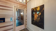 Located at 309 Mirroton Ave in Lakeland, Florida, this single-floor wellness facility is thoughtfully designed to blend aesthetic appeal with cutting-edge recovery technology. The interior opens into a stylish entryway corridor featuring rich wood-paneled walls, durable hardwood-style flooring, and an elegant multi-bulb chandelier that sets a warm, upscale tone. Curated large-scale artwork adorns the walls throughout, adding a sophisticated, gallery-like character to the space.

The entryway leads to a welcoming lobby area distinguished by soaring ceilings, a statement gold circular wall sculpture, and designer lighting that reinforces the space's modern aesthetic. A wood-framed glass door provides access to the sauna room, which is lined with natural cedar wood slat panels and fitted with tiered bench seating — a hallmark of traditional infrared or steam sauna design.

Treatment rooms are equipped with advanced therapeutic loungers and infrared body wrap beds, accompanied by integrated tablet controls for a personalized session experience. Floor-to-ceiling windows with linen privacy curtains allow natural light to filter into these rooms while maintaining a calm, retreat-like ambiance. The overall design philosophy of the space prioritizes comfort, wellness, and a clean modern aesthetic, making it well-suited for a professional recovery or med-spa environment.