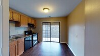 This single-floor residence offers a practical and comfortable layout across several well-defined living areas. The kitchen is efficiently designed, featuring warm honey-toned wood cabinetry, dark granite-style countertops, and a full suite of black appliances including a refrigerator, electric range, dishwasher, and built-in microhood. Dark hardwood-style flooring runs throughout the kitchen and dining area, adding a rich contrast to the neutral taupe walls. A sliding glass door in the dining area floods the space with natural light and provides direct access to an outdoor deck overlooking a wooded backdrop.

The living areas are carpeted in a neutral tan tone, offering a soft and inviting feel. Large multi-pane windows are present throughout, allowing generous natural light to penetrate each room and offering outdoor views of the surrounding landscape. The bedrooms are spacious and well-lit, with one room featuring a floor-to-ceiling built-in closet system that provides substantial storage capacity.

The bathroom is clean and functional, equipped with a white vanity, toilet, and a tub-shower combination enclosed by sliding frosted glass doors with chrome framing. The consistent use of warm neutral tones throughout the space creates a cohesive and understated aesthetic from room to room.