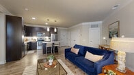 Located at 3600 Park East Dr in Beachwood, OH, this well-appointed one-bedroom, one-bathroom unit offers a thoughtfully designed open-concept layout that maximizes its efficient footprint. The combined kitchen and living area serves as the heart of the home, featuring wood-style plank flooring, neutral tones, and large sliding glass doors that invite natural light. The kitchen is outfitted with rich dark cabinetry, a white subway tile backsplash, light stone-finish countertops, a center island with bar seating, and a full suite of stainless steel appliances including a refrigerator, range, and microwave. Pendant lighting over the island adds a modern, polished touch. The living area flows seamlessly from the kitchen, offering ample space for both lounging and dining. The bedroom is a calm retreat featuring plush carpeting, dual windows with blinds, and a ceiling fan. It connects to a spacious walk-in closet outfitted with built-in shelving, hanging rods, and dedicated storage compartments. The bathroom is clean and contemporary, with a glass-enclosed walk-in shower, white tile surround, and tiled flooring. A hallway provides additional separation and privacy between living and sleeping areas, completing this cohesive and functional layout.